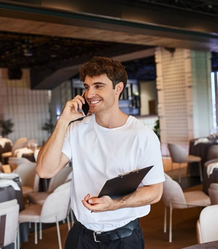 smiling-event-organizer-with-clipboard-talking-on-smartphone-near-festive-tables-in-banquet-hall.jpg
